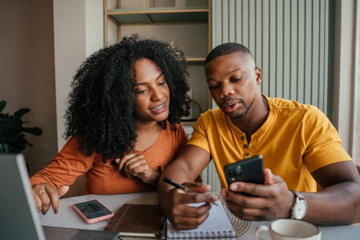 young couple with a calculator, laptop and notepads working together at a kithcen table