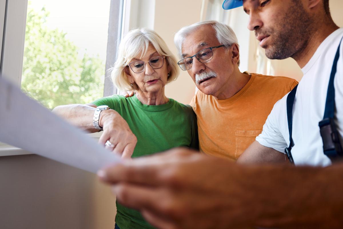 senior couple analyzing housing plans with an installation worker in their apartment