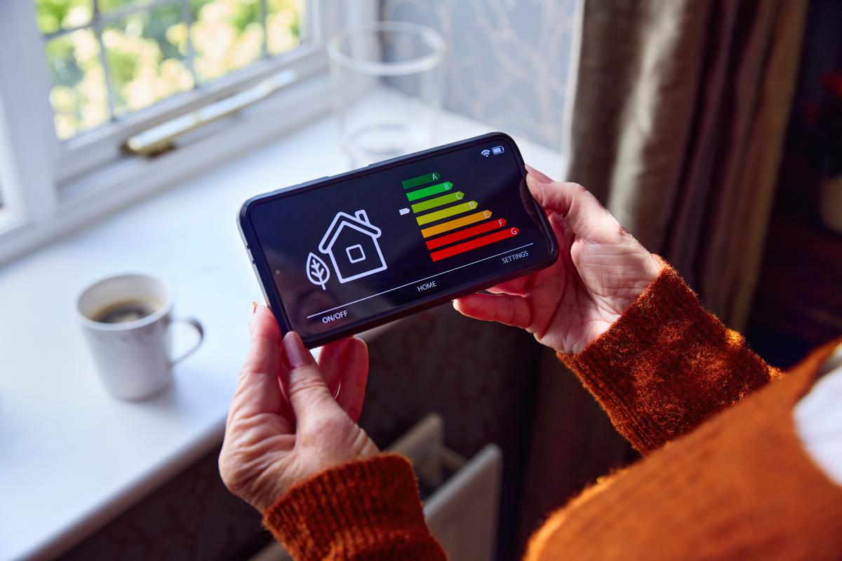 senior woman holding a smart meter by a window with a cup of coffee