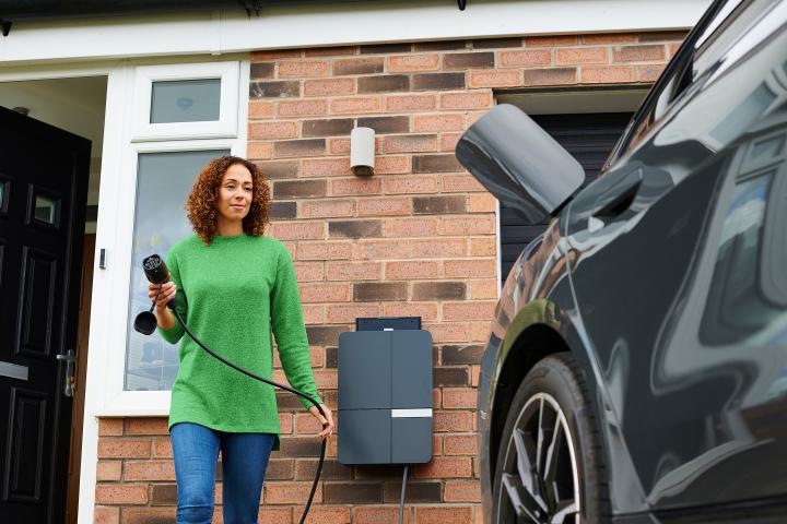 smiling woman charging an electric car on a home driveway