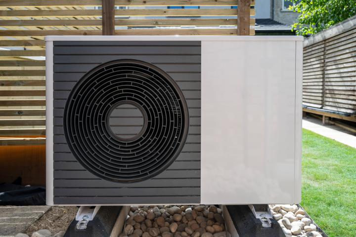 front view of the air source heat pump outside in the garden, near wooden fence on a sunny day
