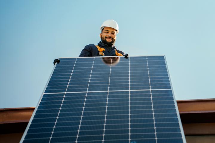 worker holding on a roof installing a solar panel