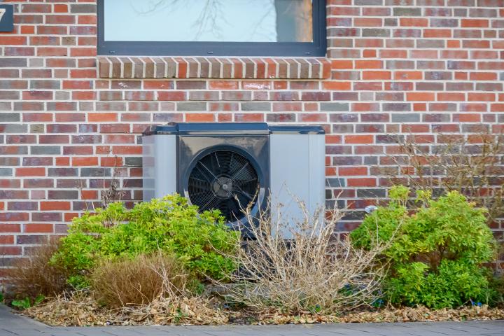 air-source heat pump mounted on brick wall with garden landscaping.