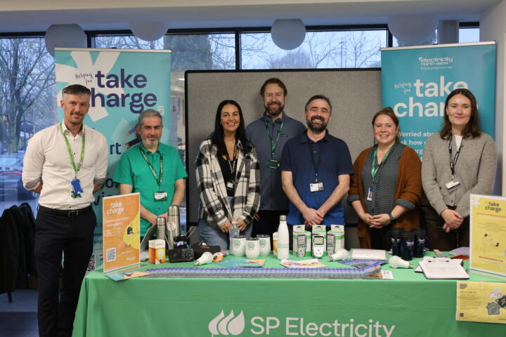 A picture of the Take Charge stand at The Senator Group employee wellbeing day. 3 smiling Senator Group employees are standing alongside the Take Charge team, behind the stand.